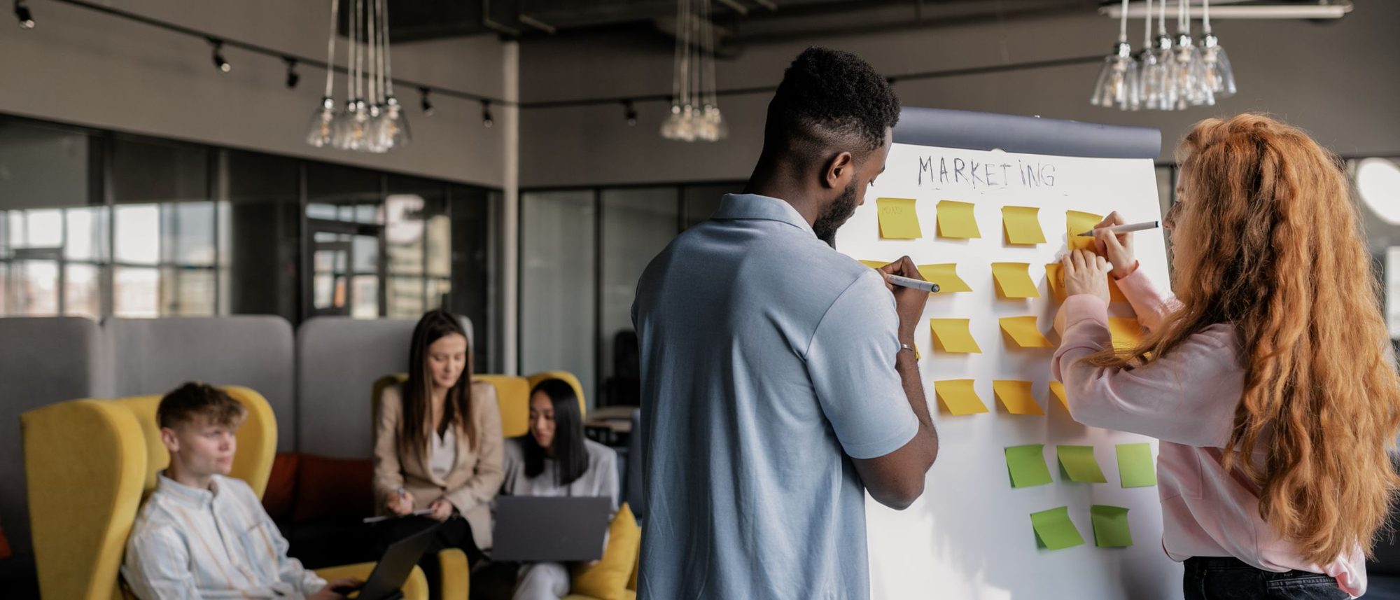 Two colleagues planning with sticky notes on a whiteboard in a bright, open office